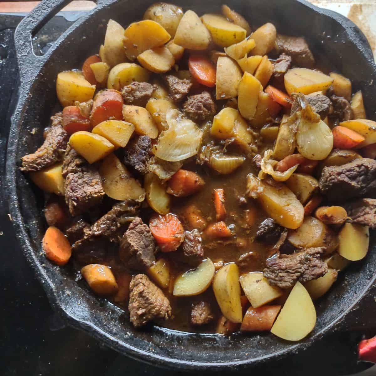 A finished beef stew with carrots, potatoes, and pearl onions.