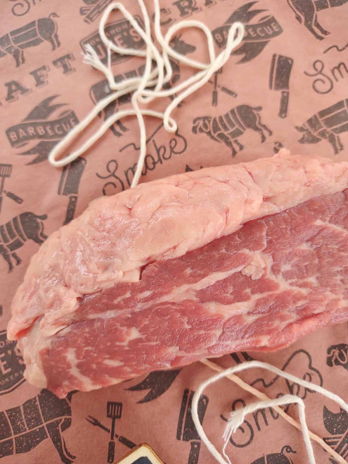 A raw Newport steak on a piece of butcher paper with string underneath the steak. The picture is zoomed in on the fat cap on the top part of the steak.