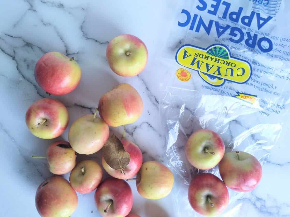Crimson Gold apples laying loose on a white surface with an empty bag from Cuyama Orchards nearby.