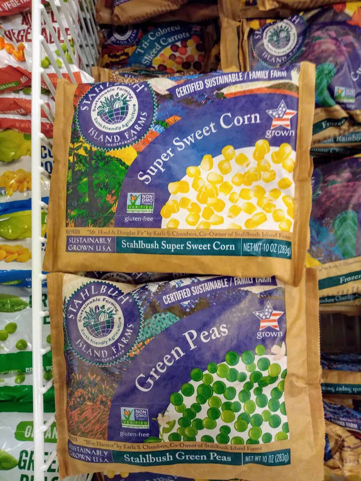 Frozen Super sweet corn and green peas in brown bags in the freezer section of a grocery store.