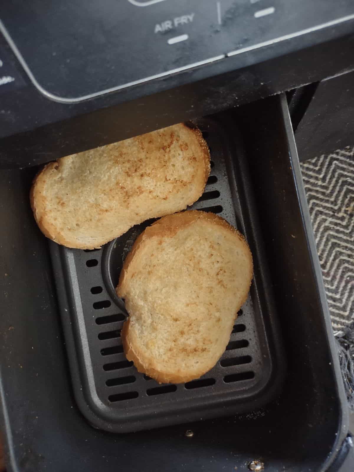 Ninji Foodi air fryer basket opened up with two pieces of garlic bread inside.