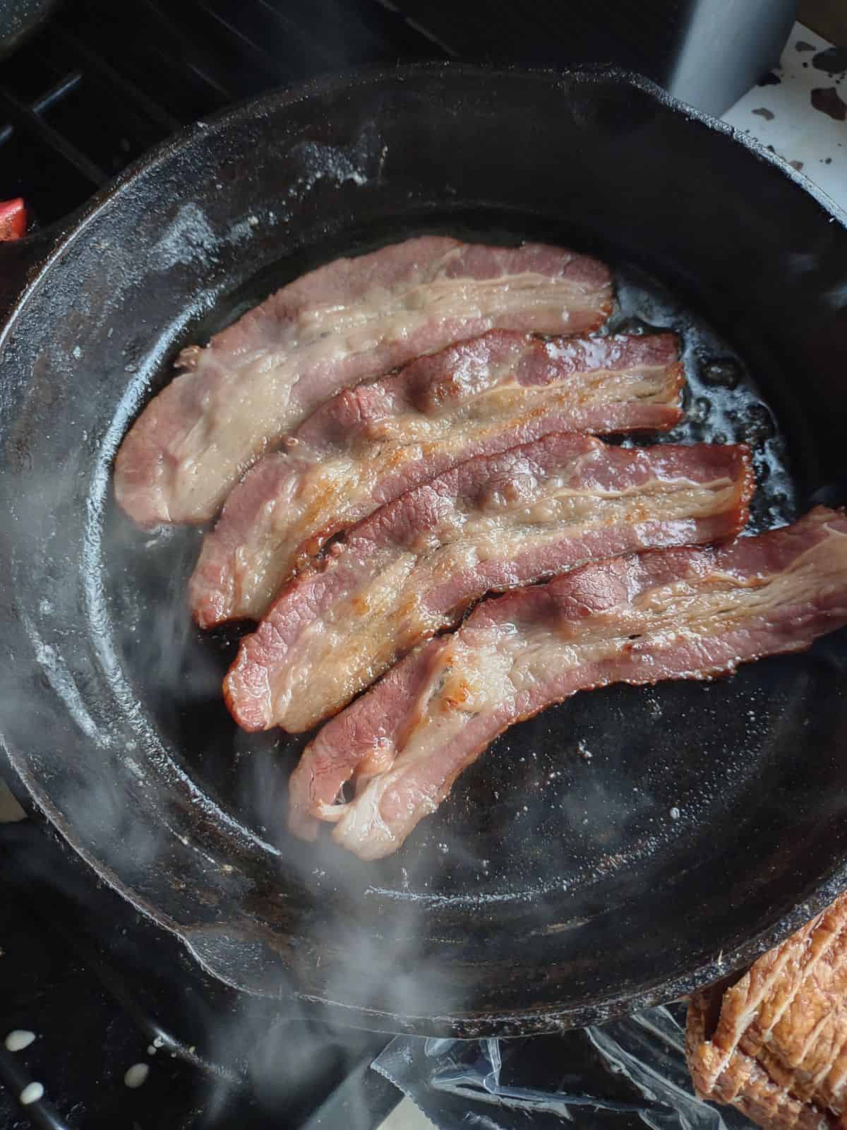Beef bacon cooking in a cast iron pan.