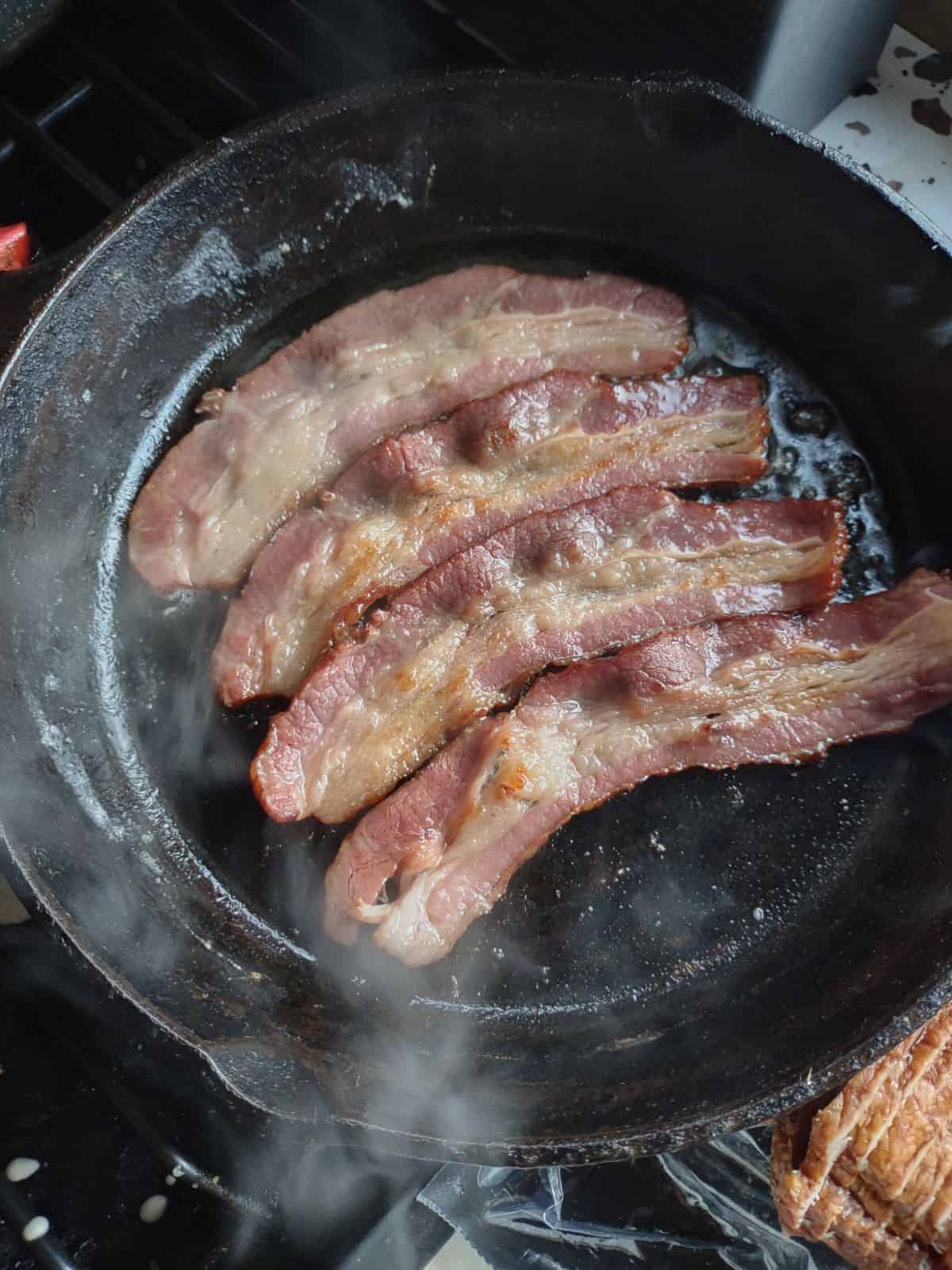 A cast iron skillet with raw bacon in it.