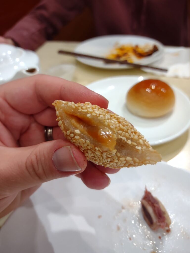 Dim Sum at a Chinese restaurant. A sesame bun is being held up showing the filling inside. 