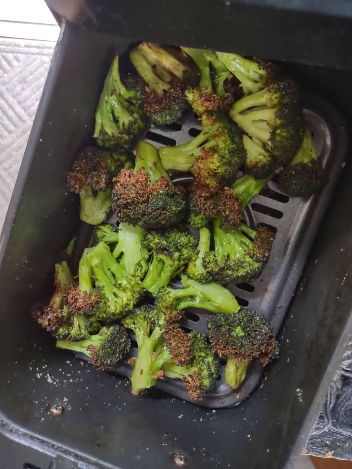 Finish broccoli in a black air fryer basket. The broccoli is browned at the tips. 