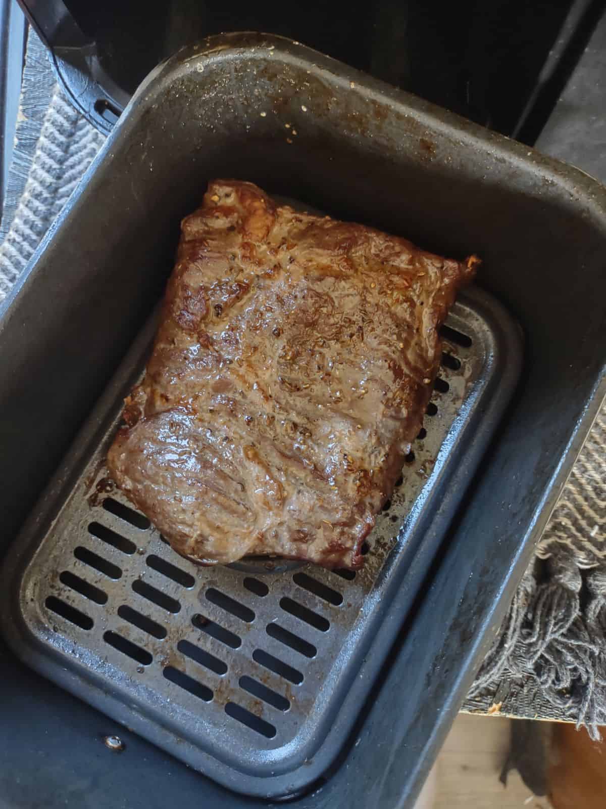 A cooked skirt steak inside a black air fryer basket.