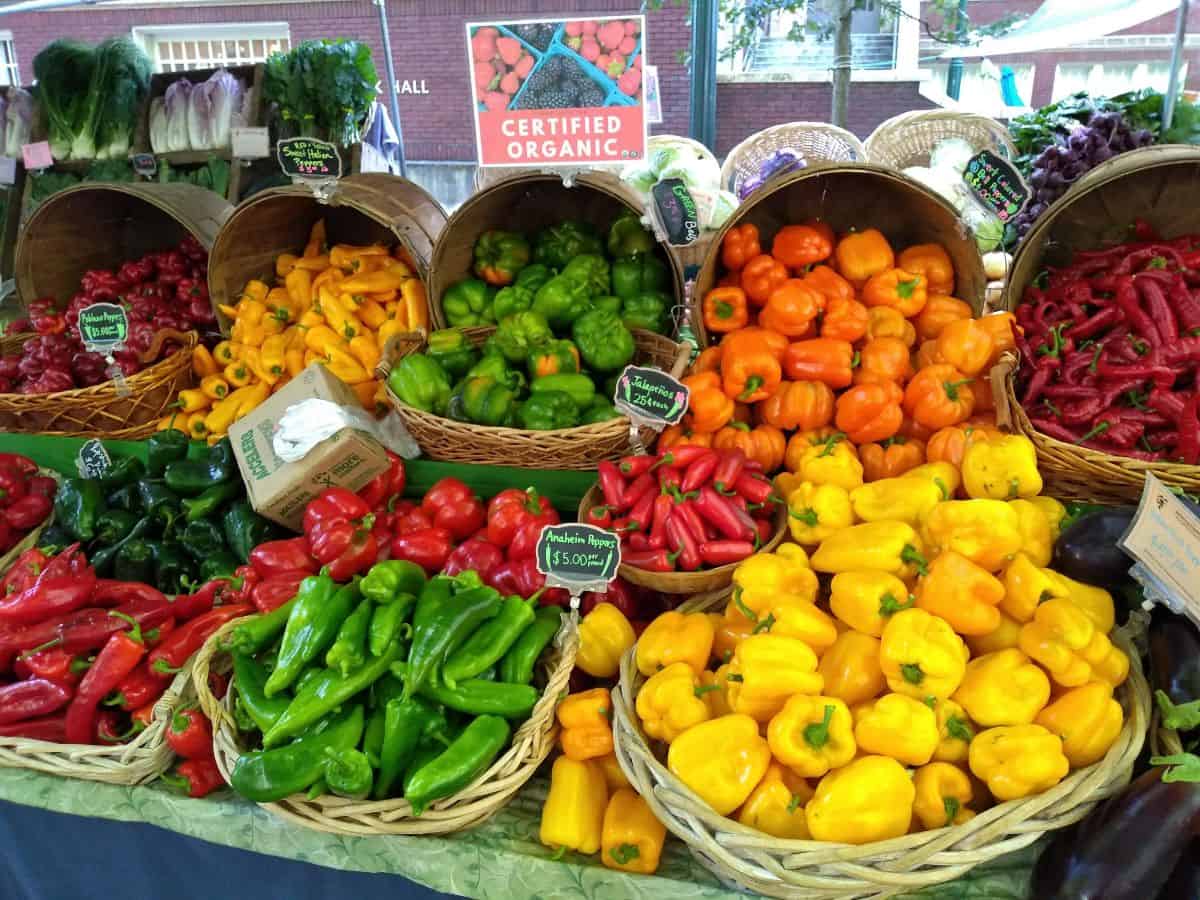 A farmer's market display of baskets of all different colored pepper, include long red sweet peppers.
