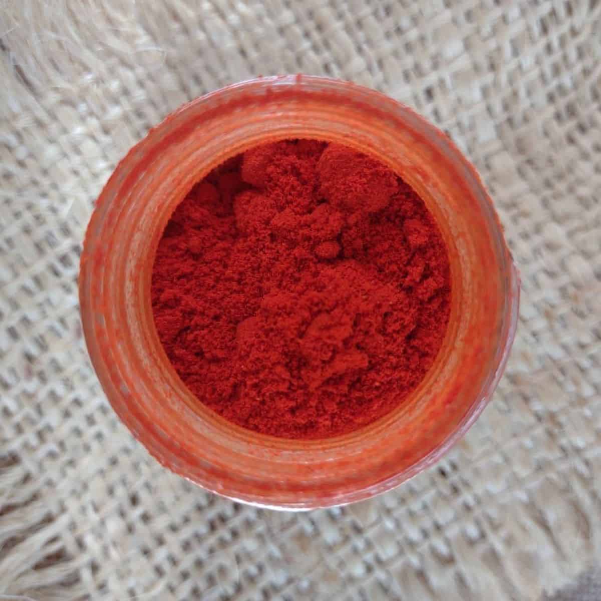 An open jar of red paprika sitting on a piece of burlap.