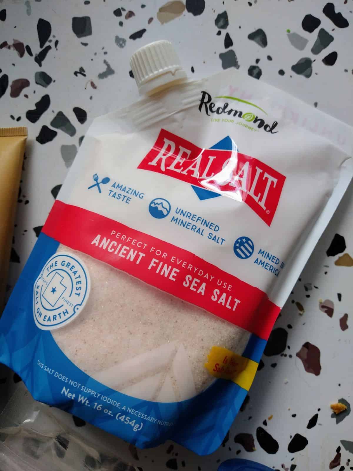 A bag of Redmond Real Salt Ancient Fine Sea Salt on a white table with spots