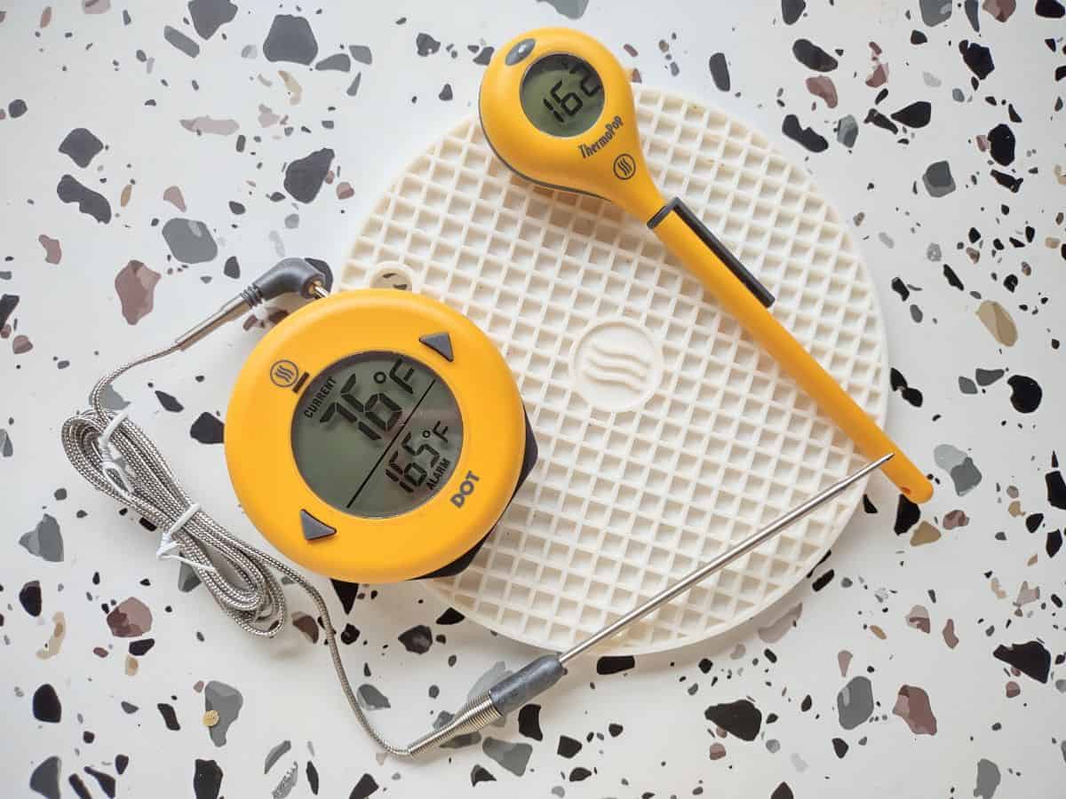 Yellow ThermWorks Dot and ThermoPop sitting on a white silicone trivet. 
