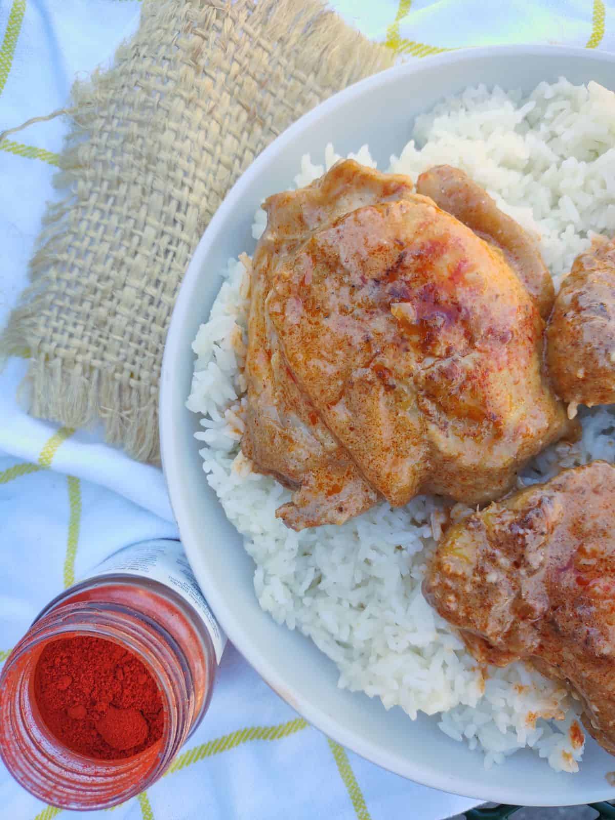 Chicken paprikash served over rice in a white bowl with an opened jar of Burlap & Barrel Noble Sweet Paprika.