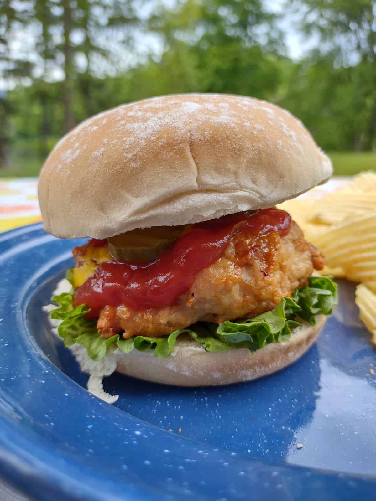 A ground chicken burger with ketchup, mustard, and lettuce outside on a picnic table.