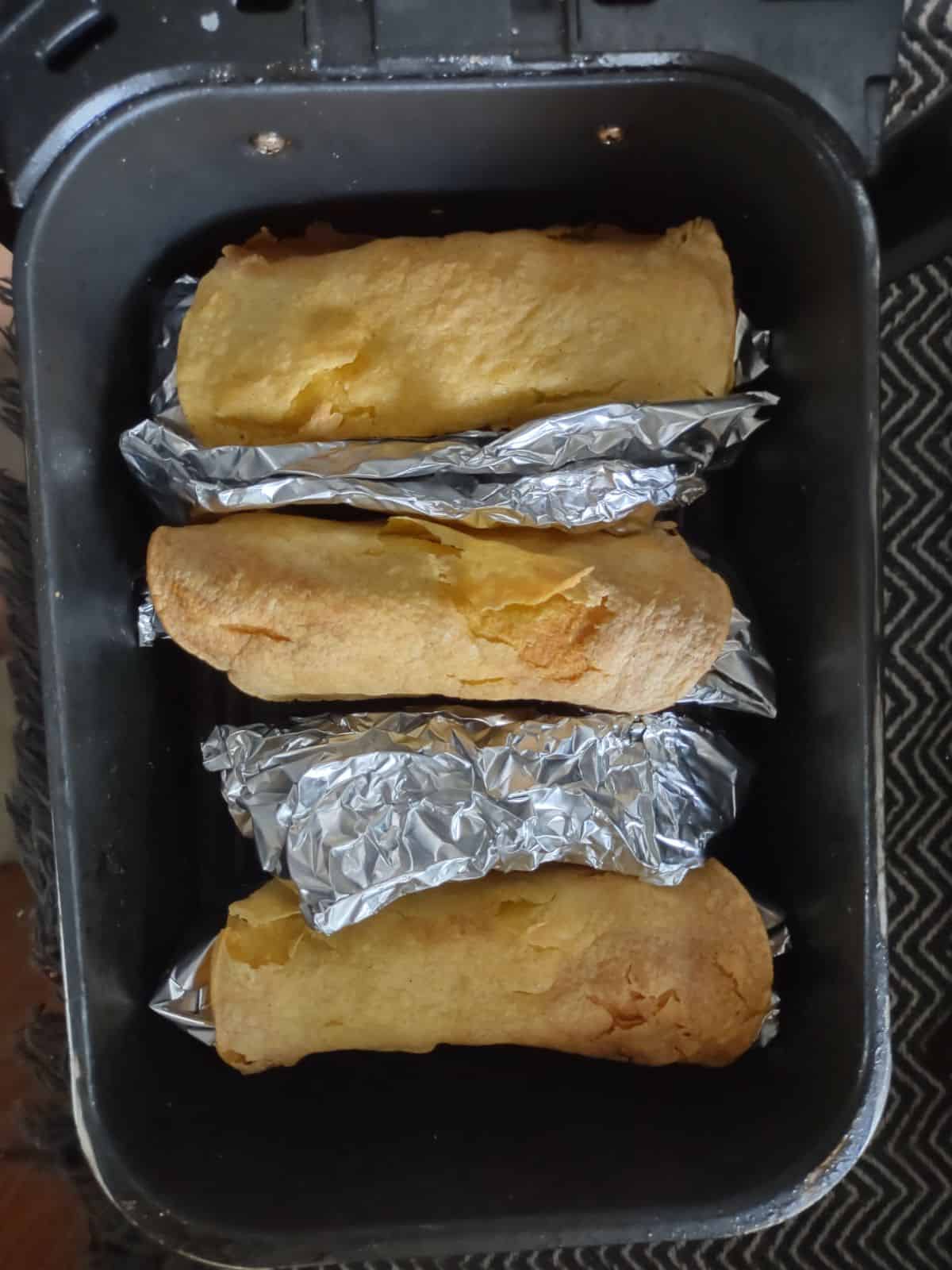 Cooked Corn tortilla that are stuffed with foil and turned upside down and placed in an air fryer basket with some foil wedges between the tortillas. 