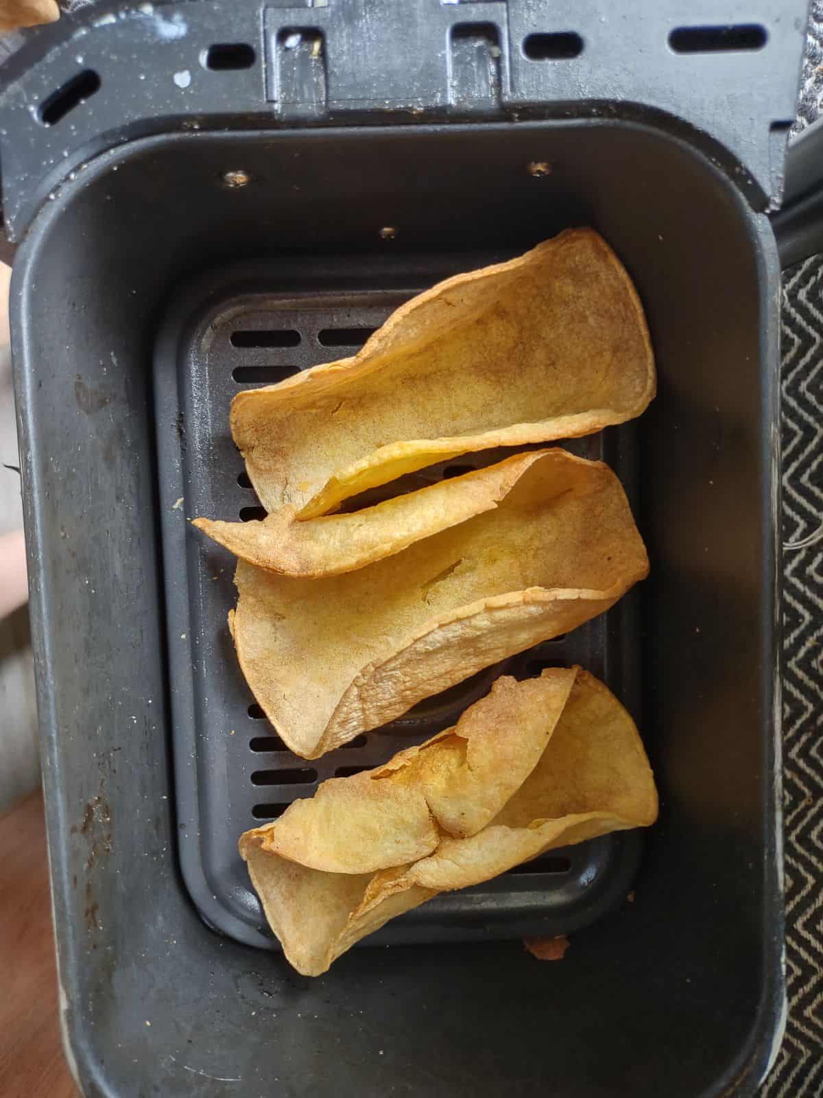 3 crunchy corn taco shells in the basket of an air fryer.