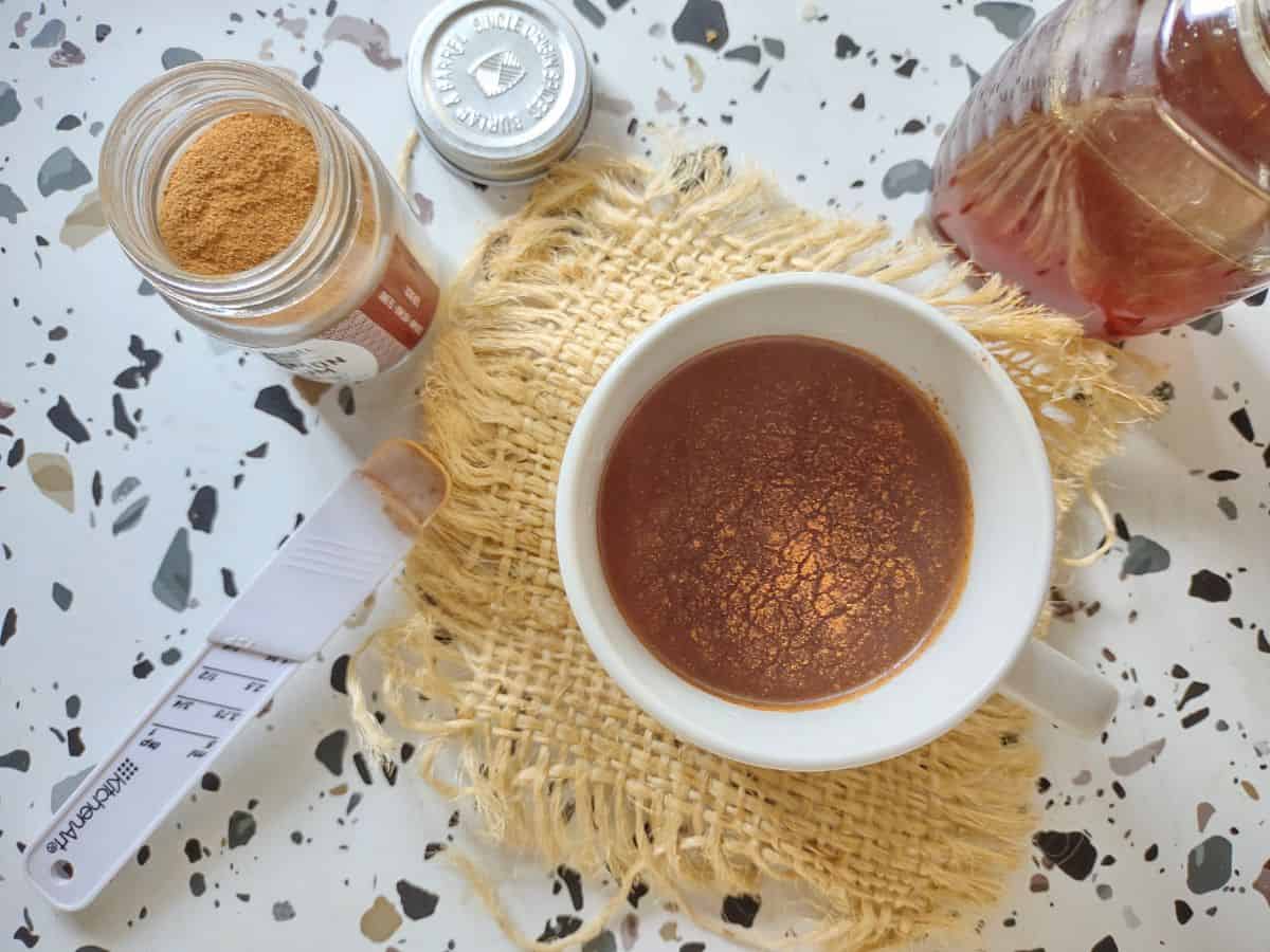 A cup of ground cinnamon tea on a piece of burlap with a jar of cinnamon and honey next to it. 