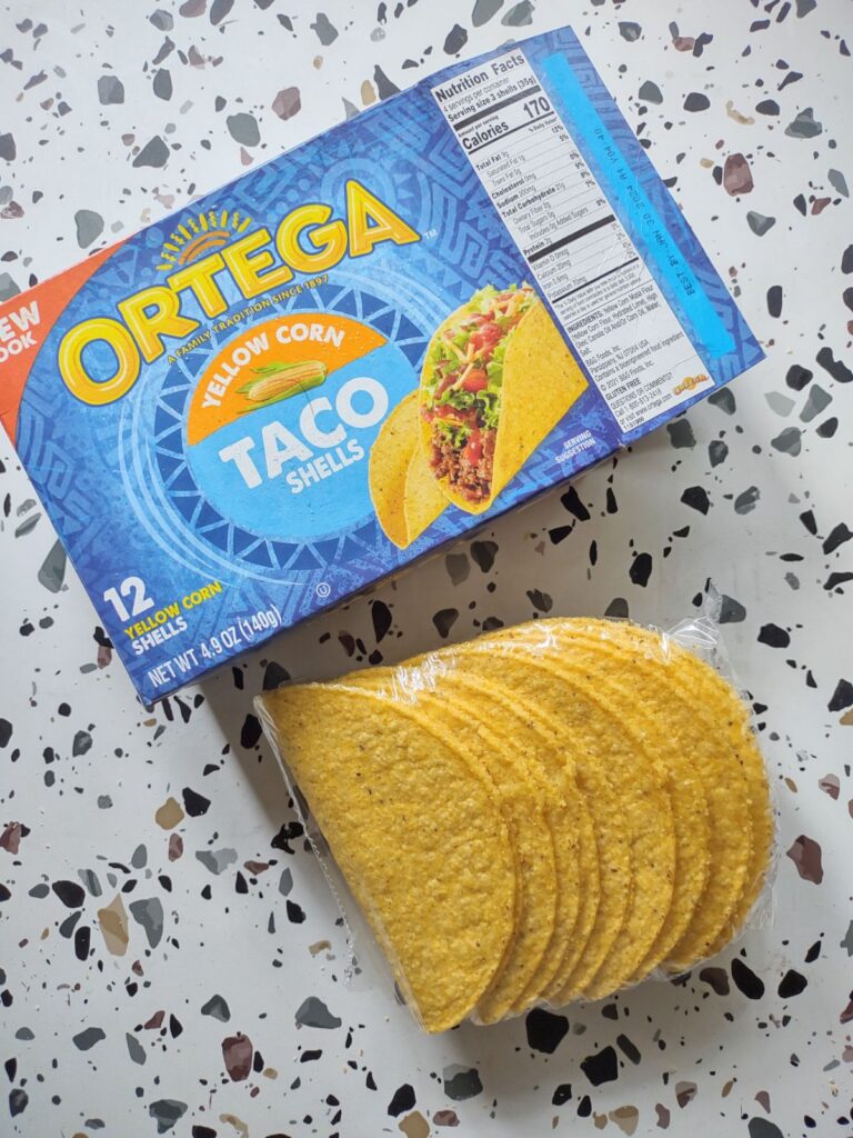 A box of Ortega Yellow Corn taco Shells that has been opened and the shells put on a table.