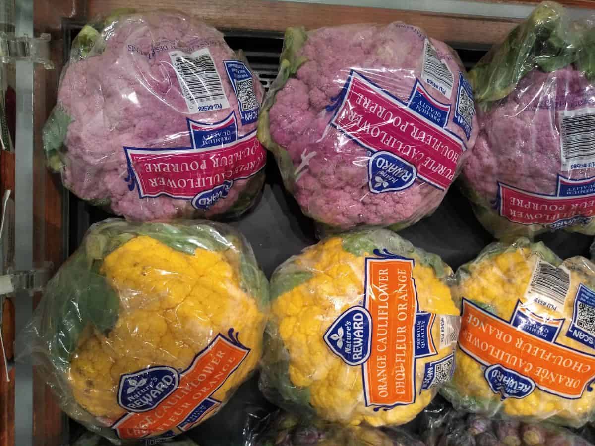 Purple and orange cauliflower heads wrapped in plastic at the store. 