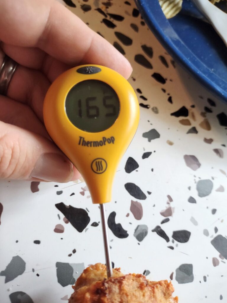 A ThermoWorks ThermoPop thermometer sticking into a chicken burger. The temperature readout says 165 degrees.