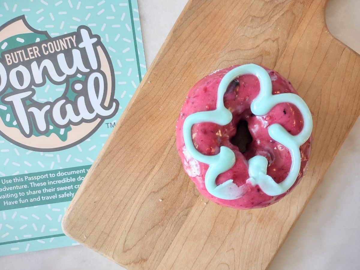 A blueberry cake donut on a wood cutting board with donut trail passport.