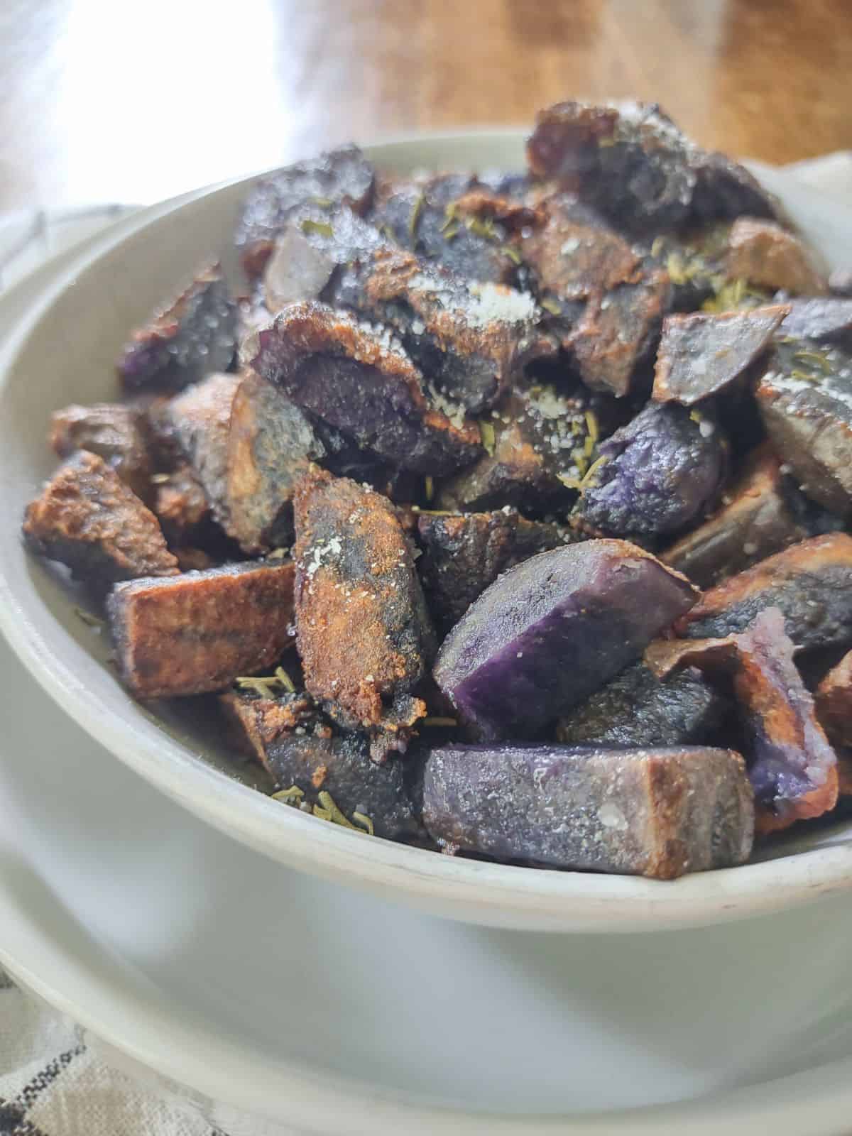 Purple potatoes that have been browed in a white bowl.