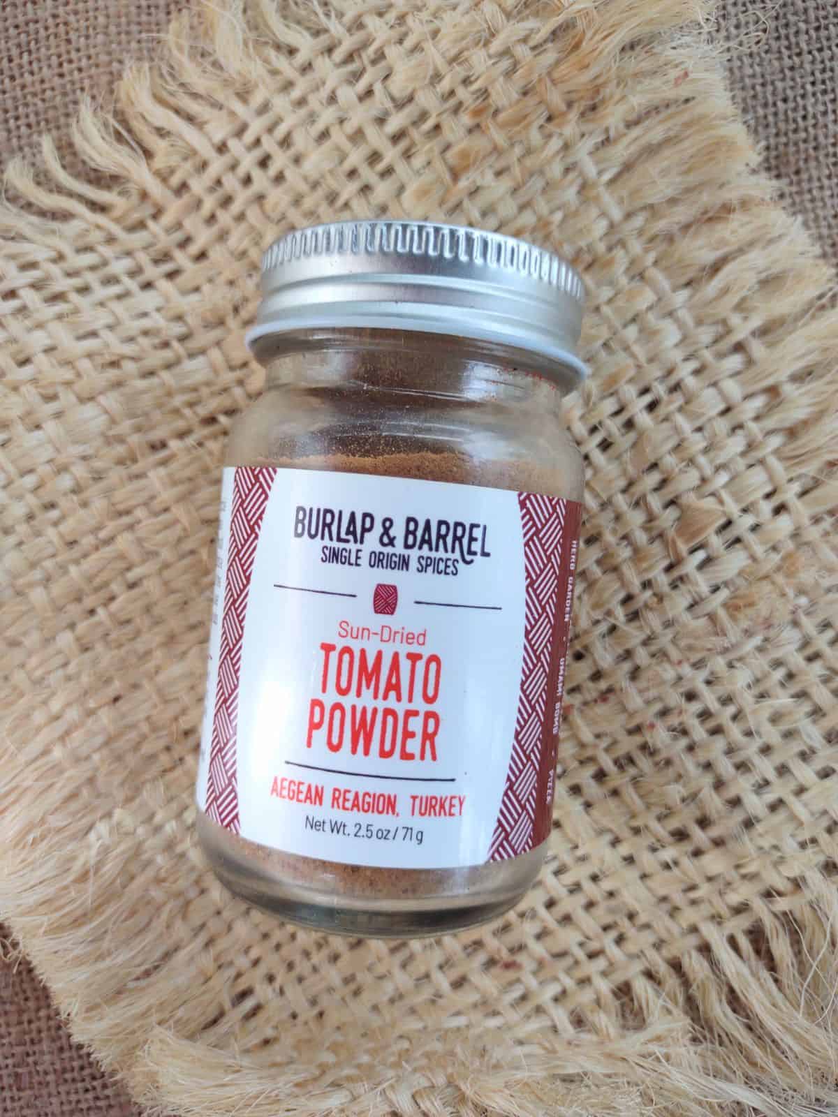 A jar of Burlap & Barrel Sun-Dried Tomato Powder on a piece of burlap.