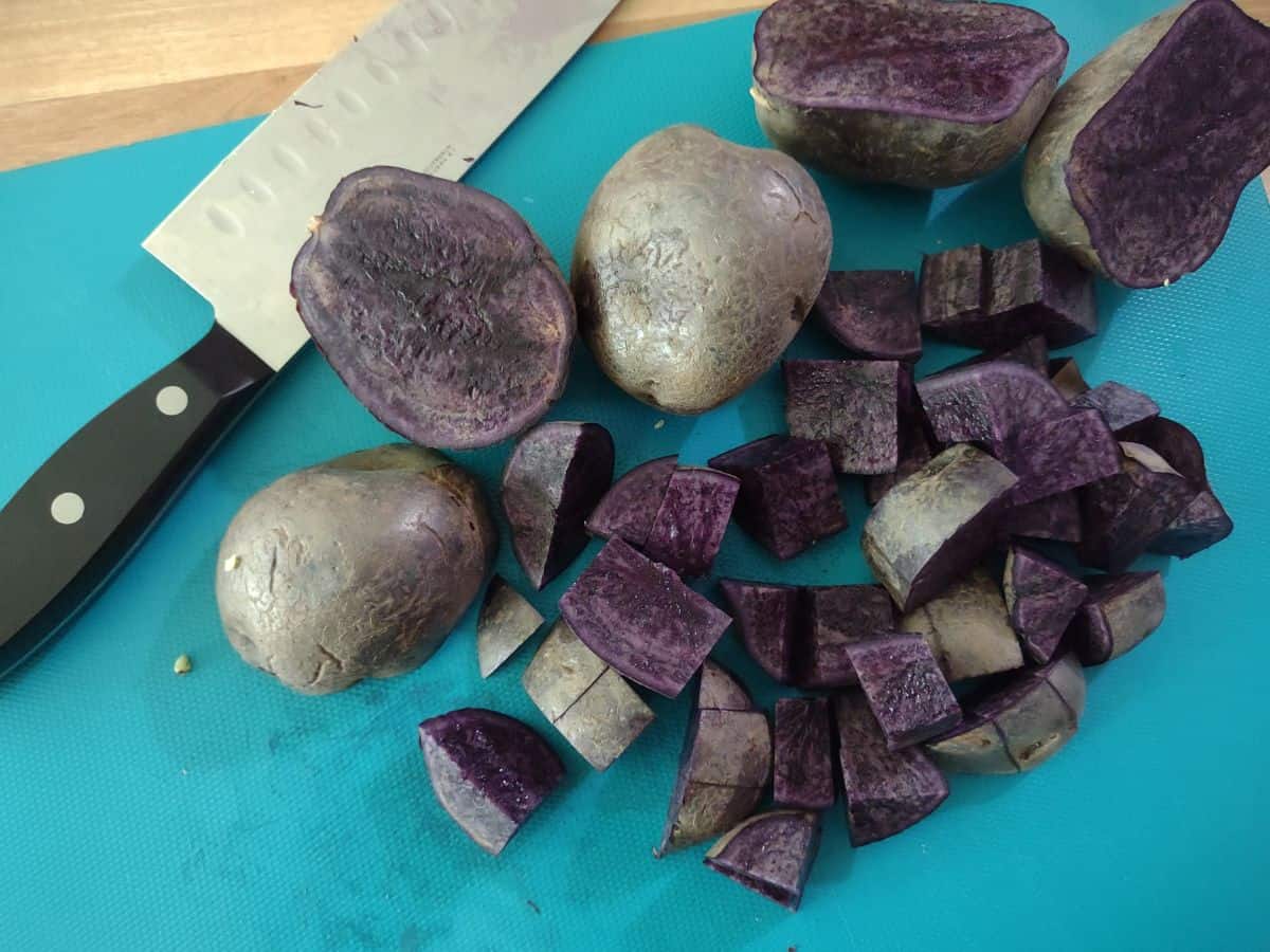 Purple potatoes cut into bite sized pieces on a blue board with a knife. 