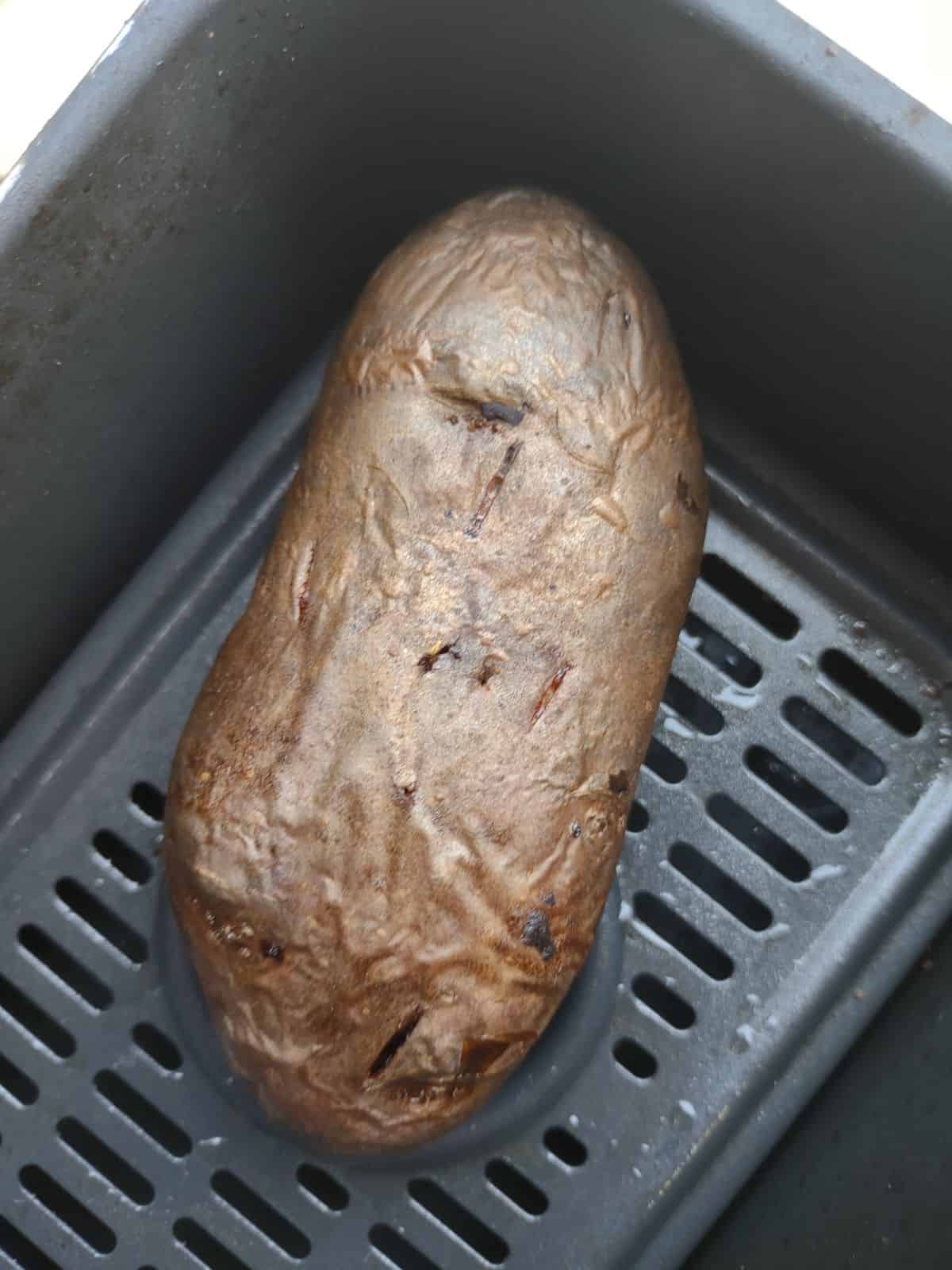 A cooked purple potato in the basket of an air fryer.