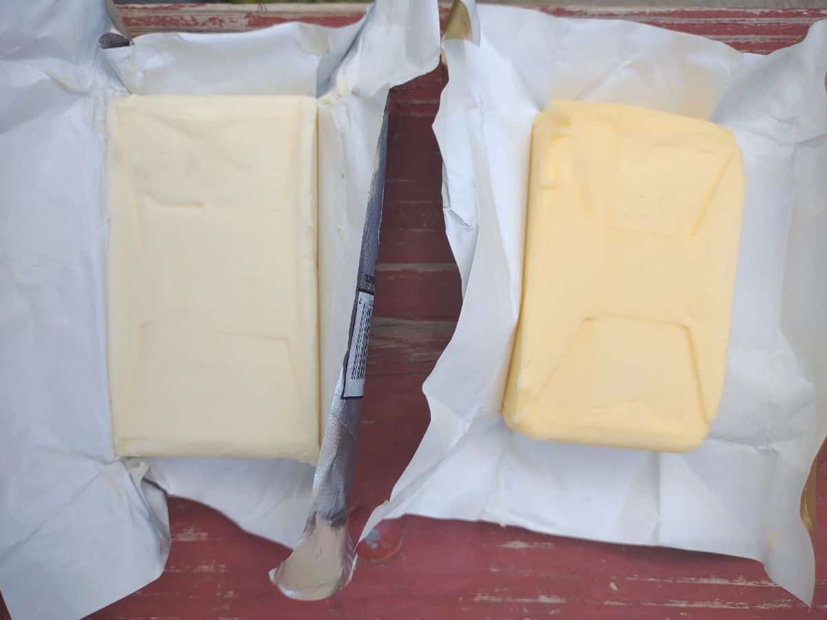 Plugra 8 oz butter next to Kerrygold 8 o butter on a red table. The Kerrygold butter is a deeper yellw color.