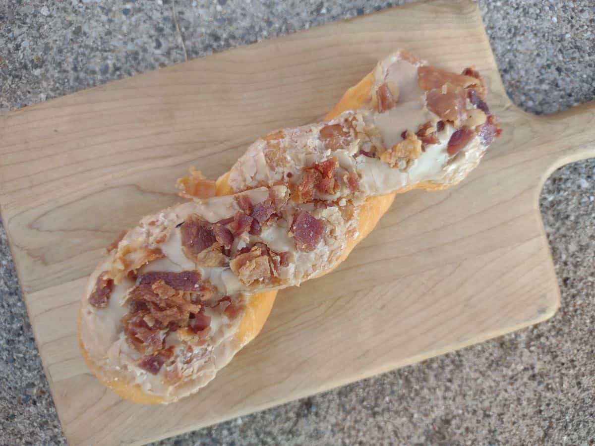 A maple bacon twist donut on a wood cutting board.