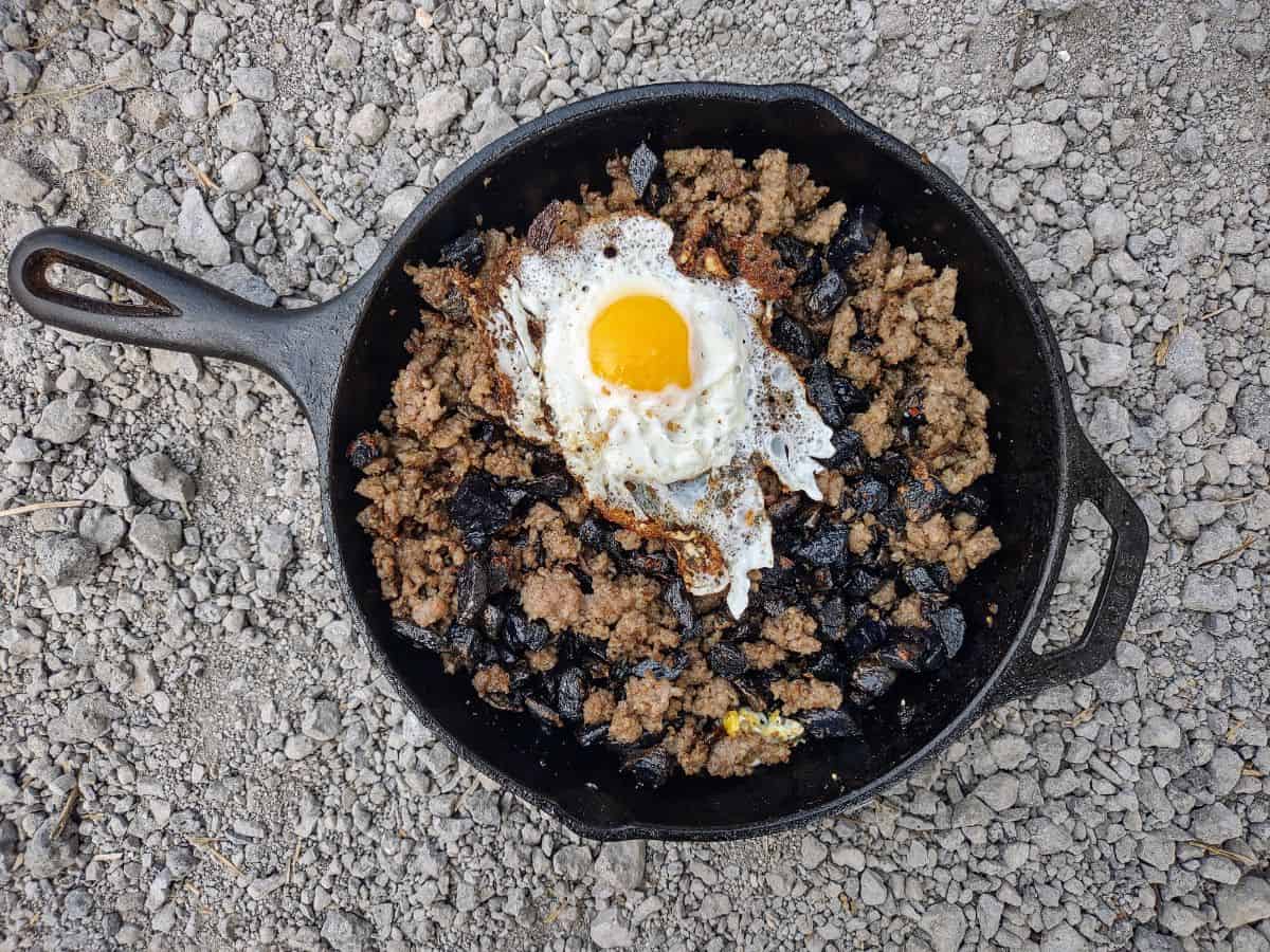 A cast iron skillet filled with ground breakfast sausage, purple potatoes, and a sunny side up egg.