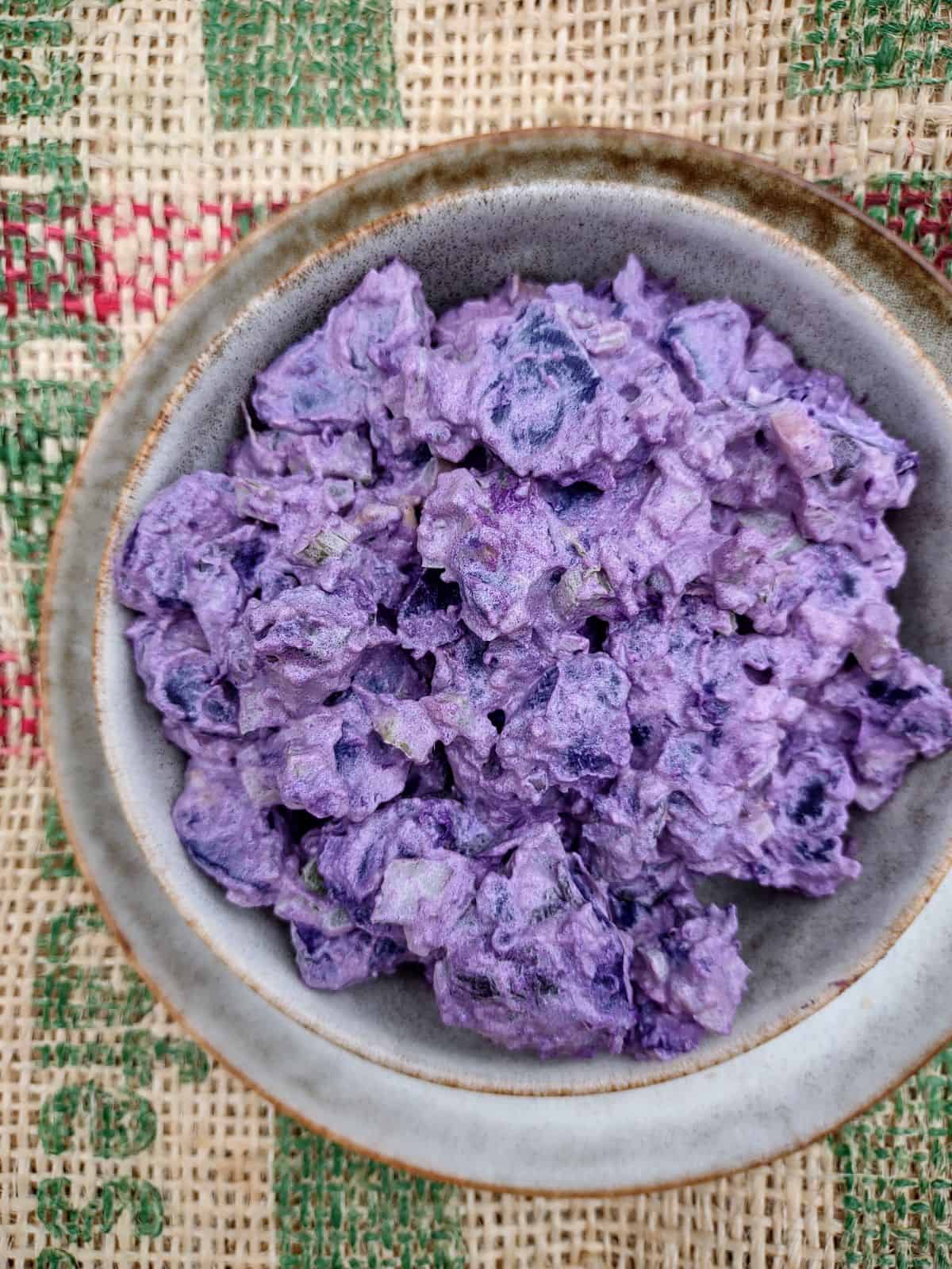 Purple potato salad in a bowl on top of a plate of the same color.
