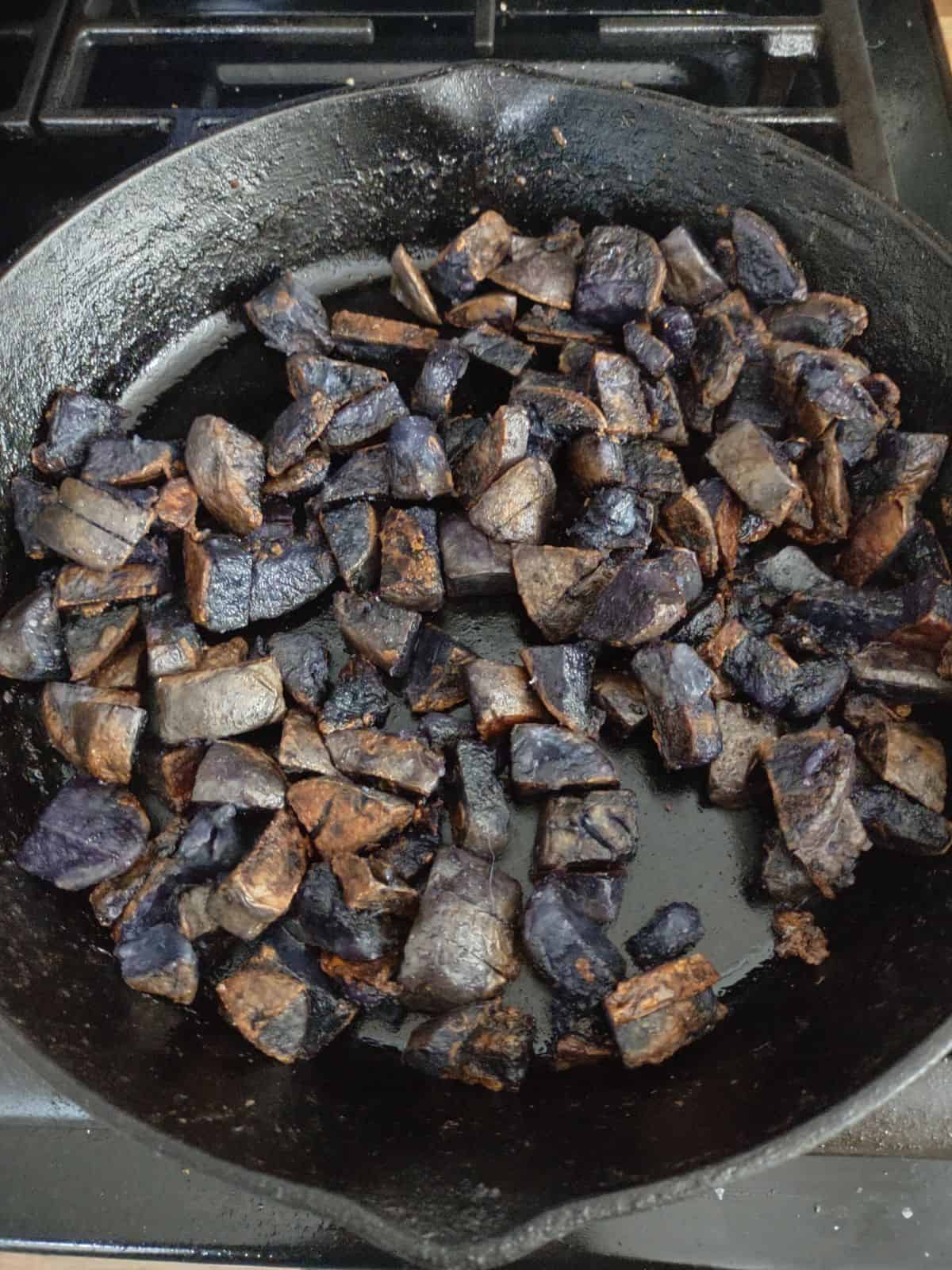 A cast iron skillet filled with purple potatoes that have been browned.