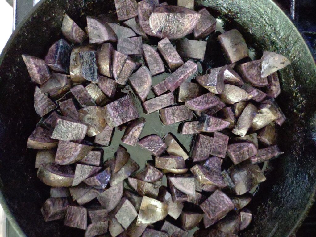 Cubed raw purple potatoes in a cast iron skillet.