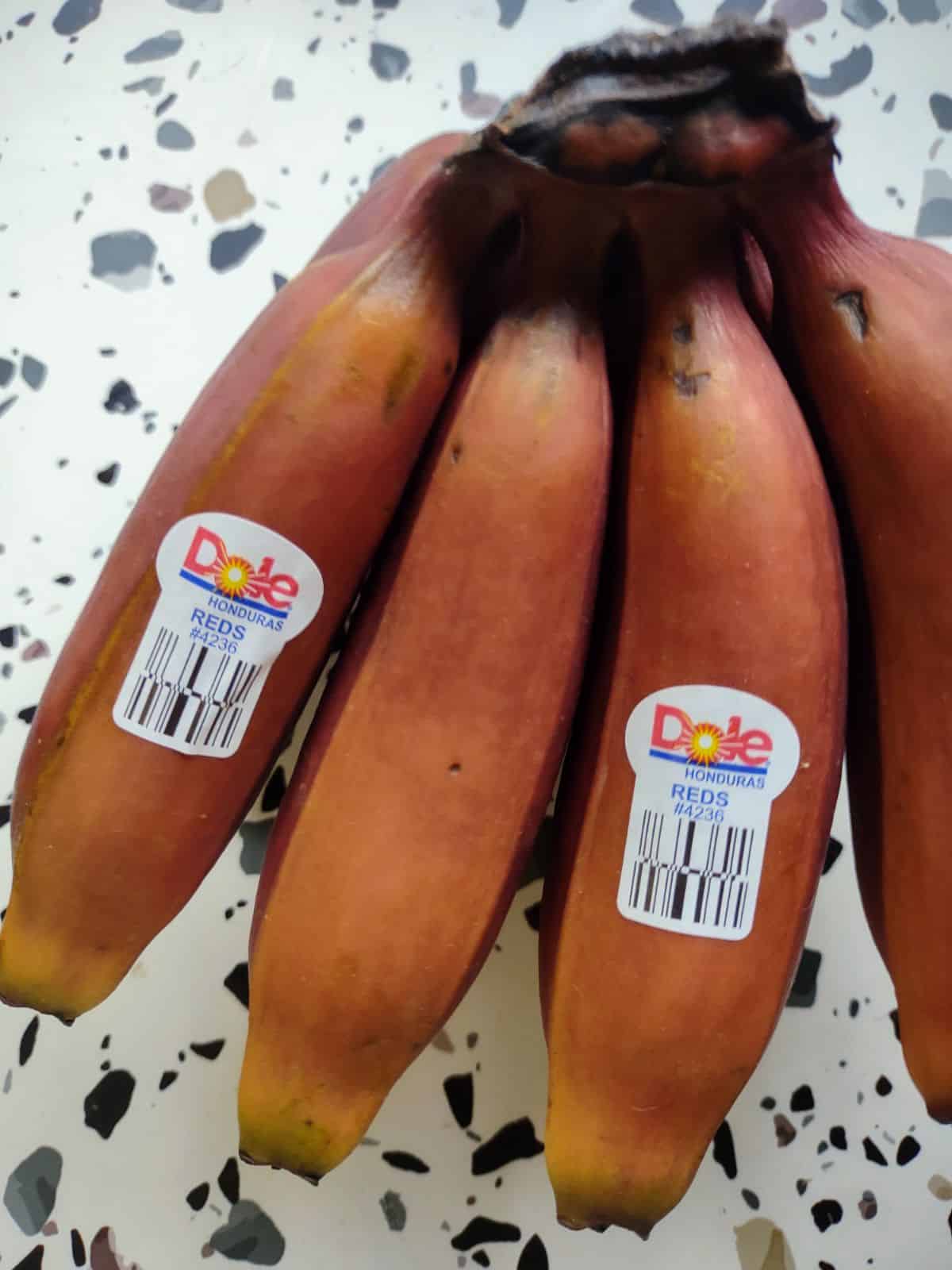 Perfectly ripe bunch of red bananas with a Dole sticker.