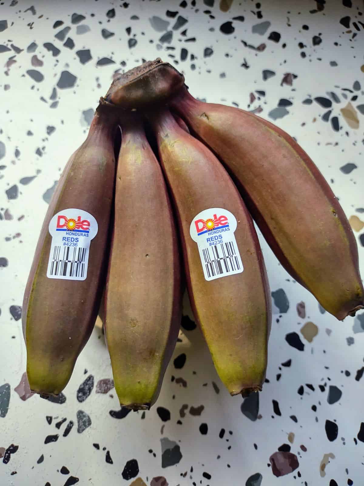 A bunch of red bananas that are unripe but starting to ripen. 