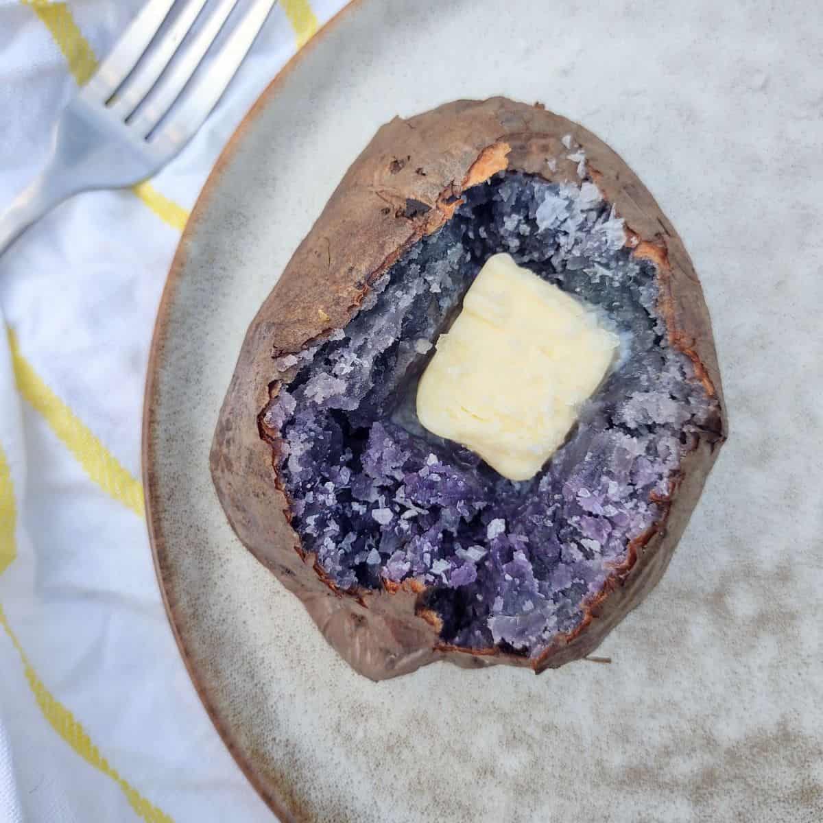 A baked purple potato opened up with a pat of butter on a plate.