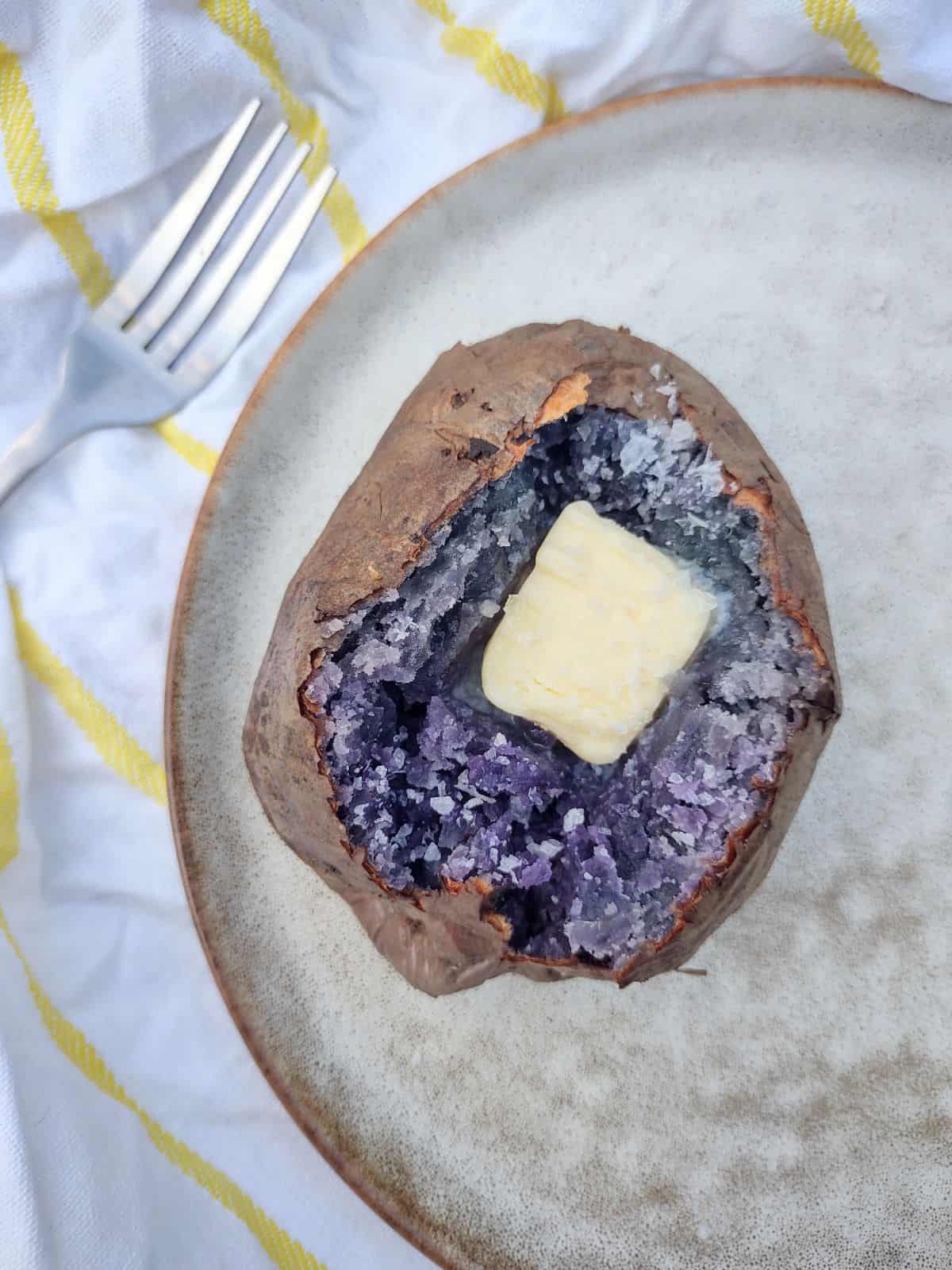 An opened baked purple potato with a pat of butter in the middle.on a plate  