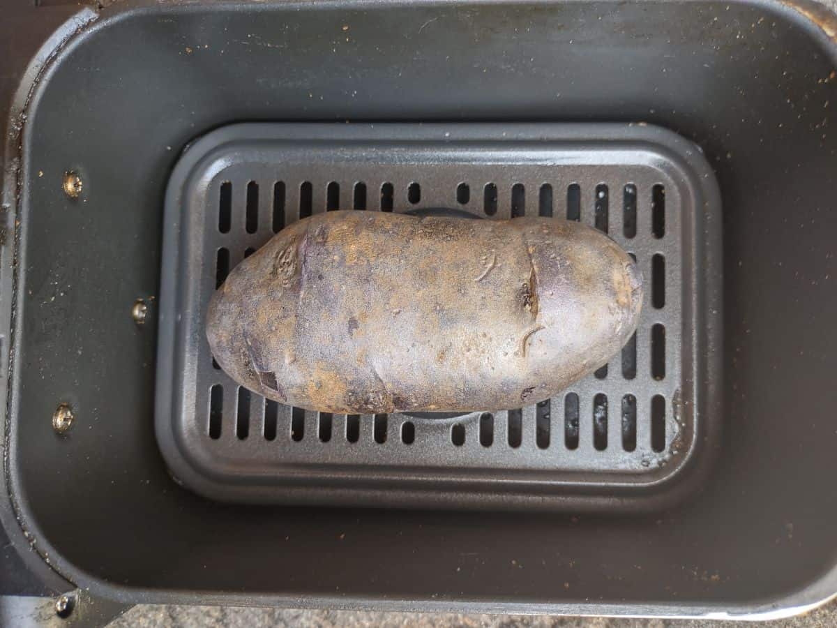 A large purple potato in an air fryer basket.