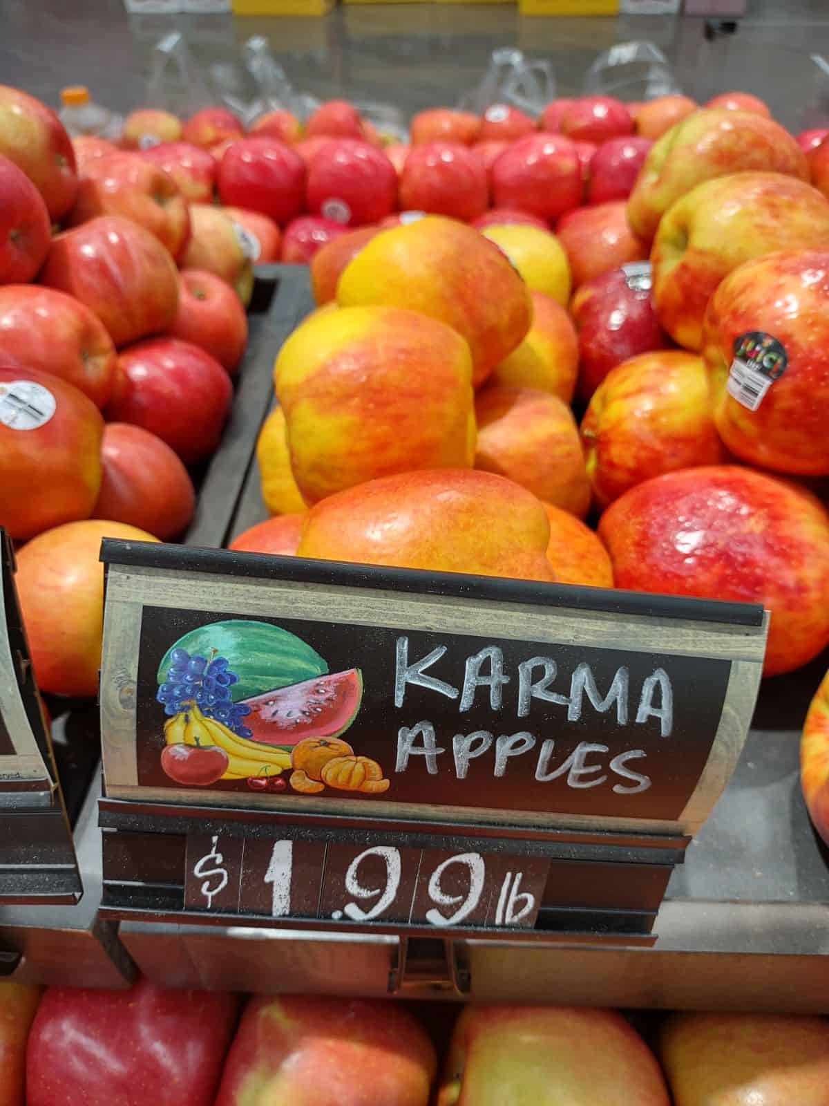 A sign that says Karma apples in front of a bunch of apples.