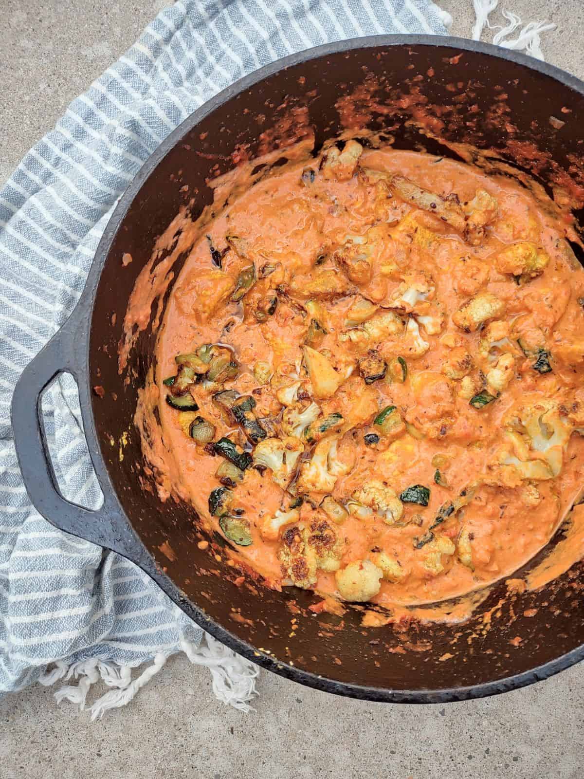 A cast iron Dutch oven filled with butter chicken with cauliflower and zucchini.