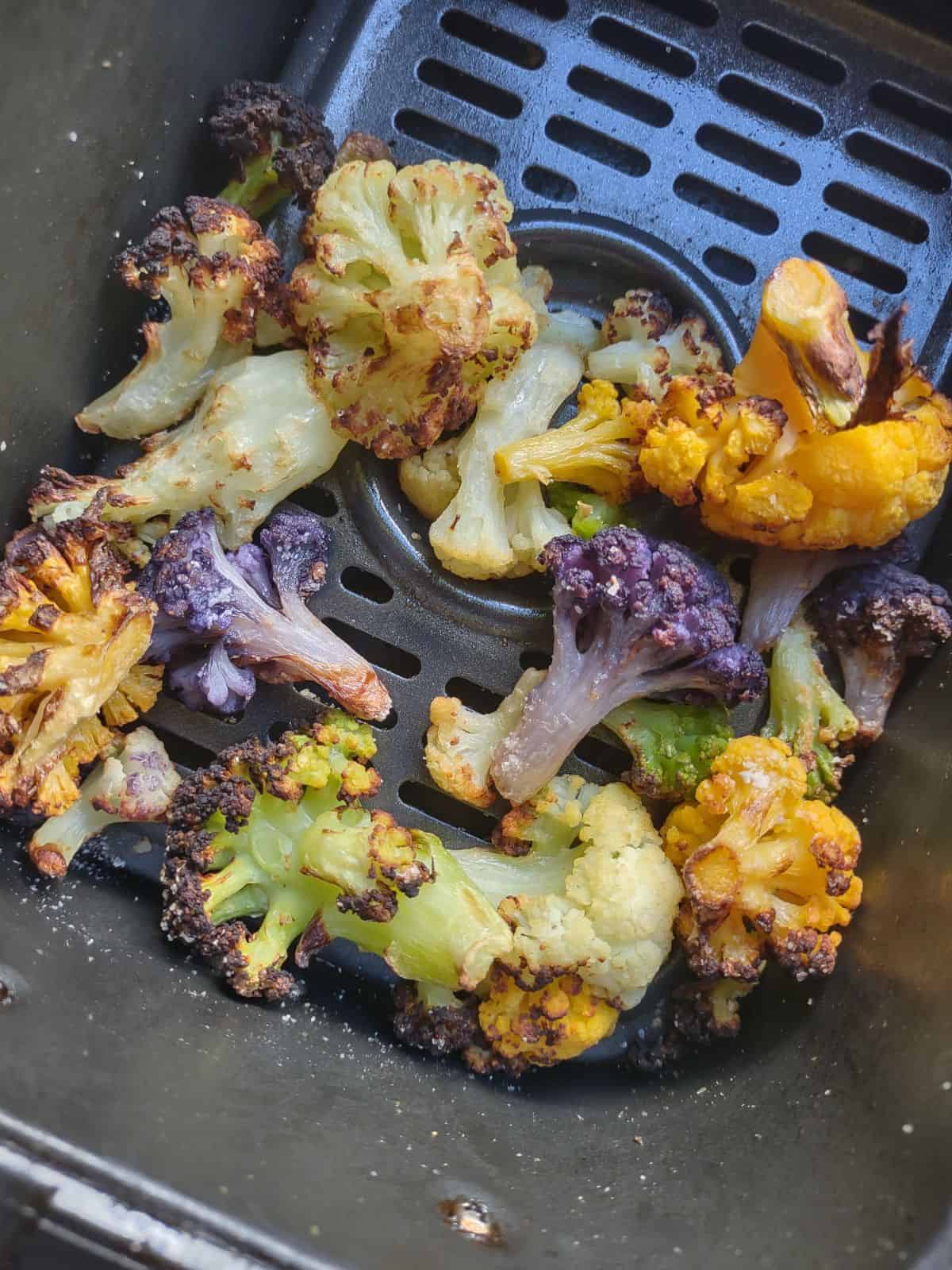 An air fryer basket with cooked rainbow Cauliflower in it. 