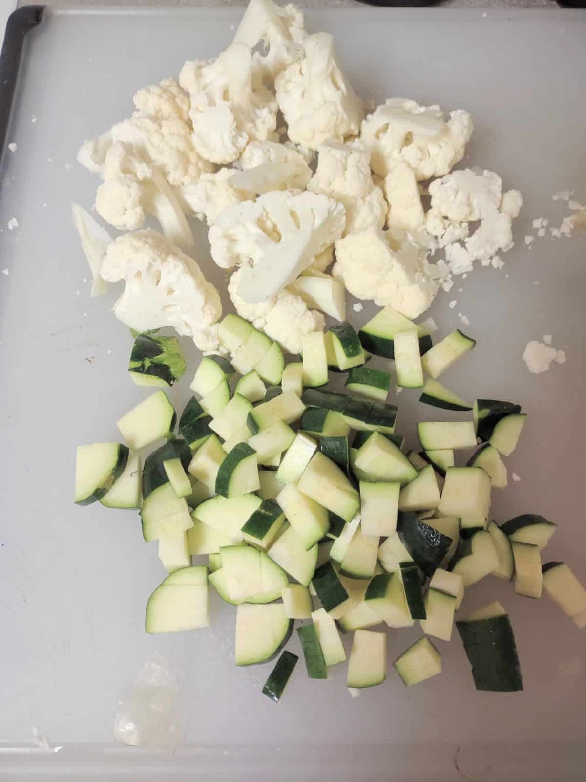 Chopped cauliflower and zucchini on a plastic cutting board.