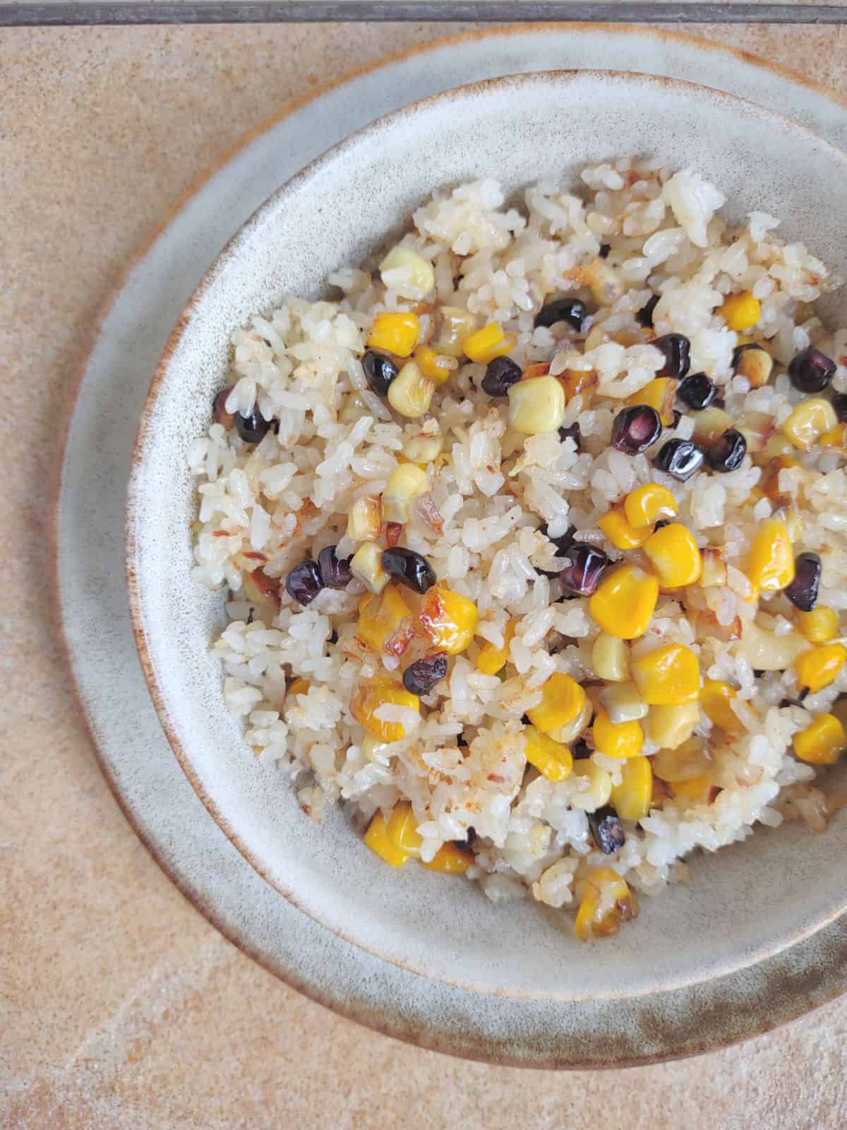 A bowl of fried rice with yellow, white, and purple corn.