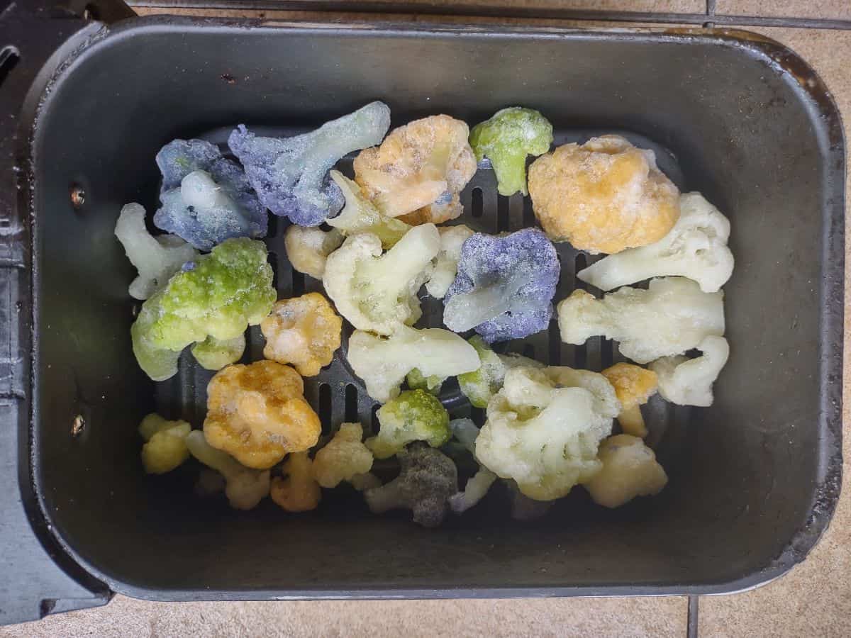 An air fryer basket with frozen rainbow Cauliflower in it.