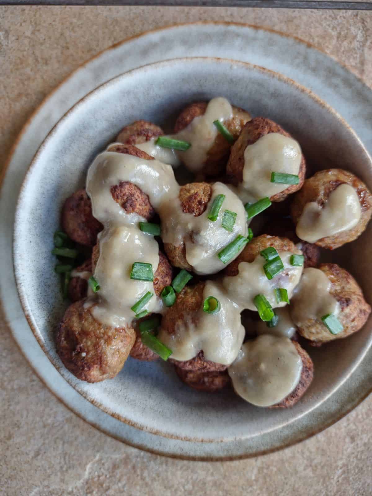 Cooked meatballs in a bowl covered in  a Swedish meatball sauce, topped with green onions.