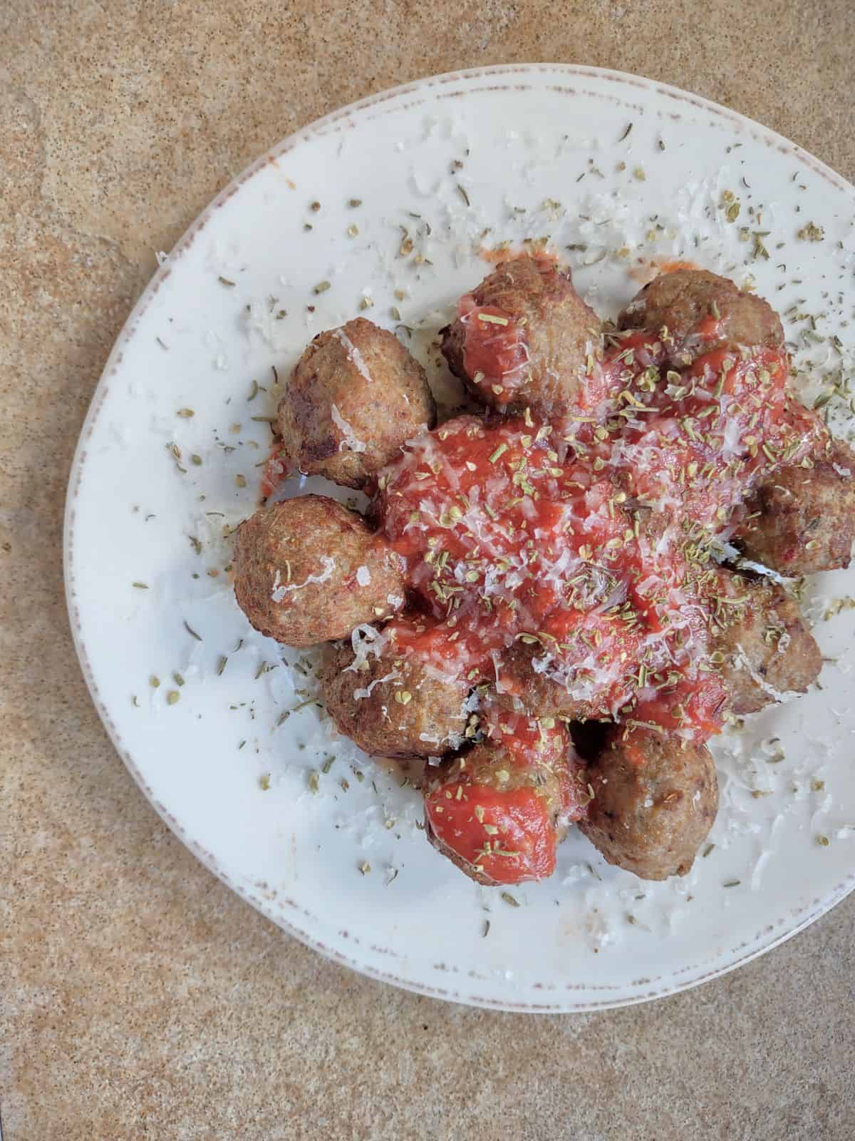 Cooked meatballs on a plate bowl covered in tomato sauce, grated parmesan cheese, and oregano.