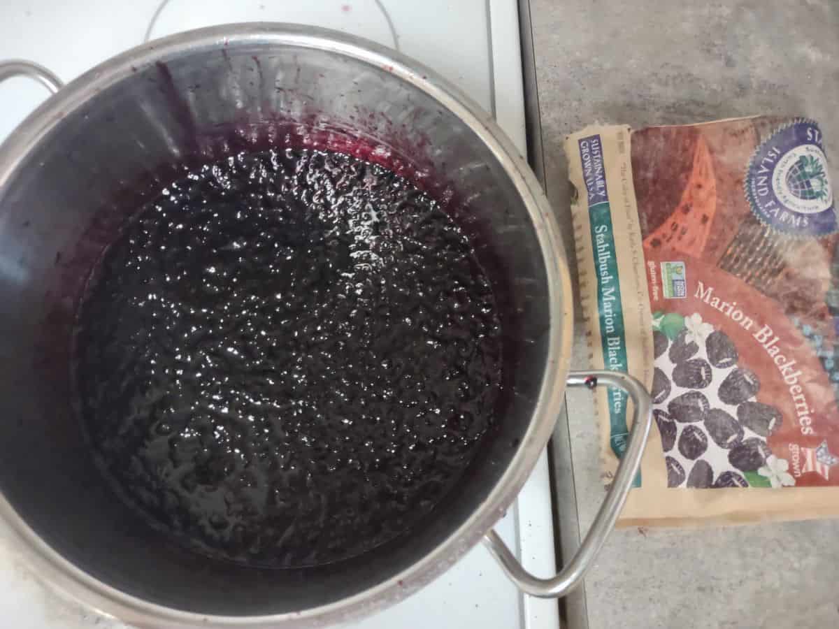 A pot of blackberry jam being cooked with a bag of Stahlbush Island farms Marion Blackberries next to it.