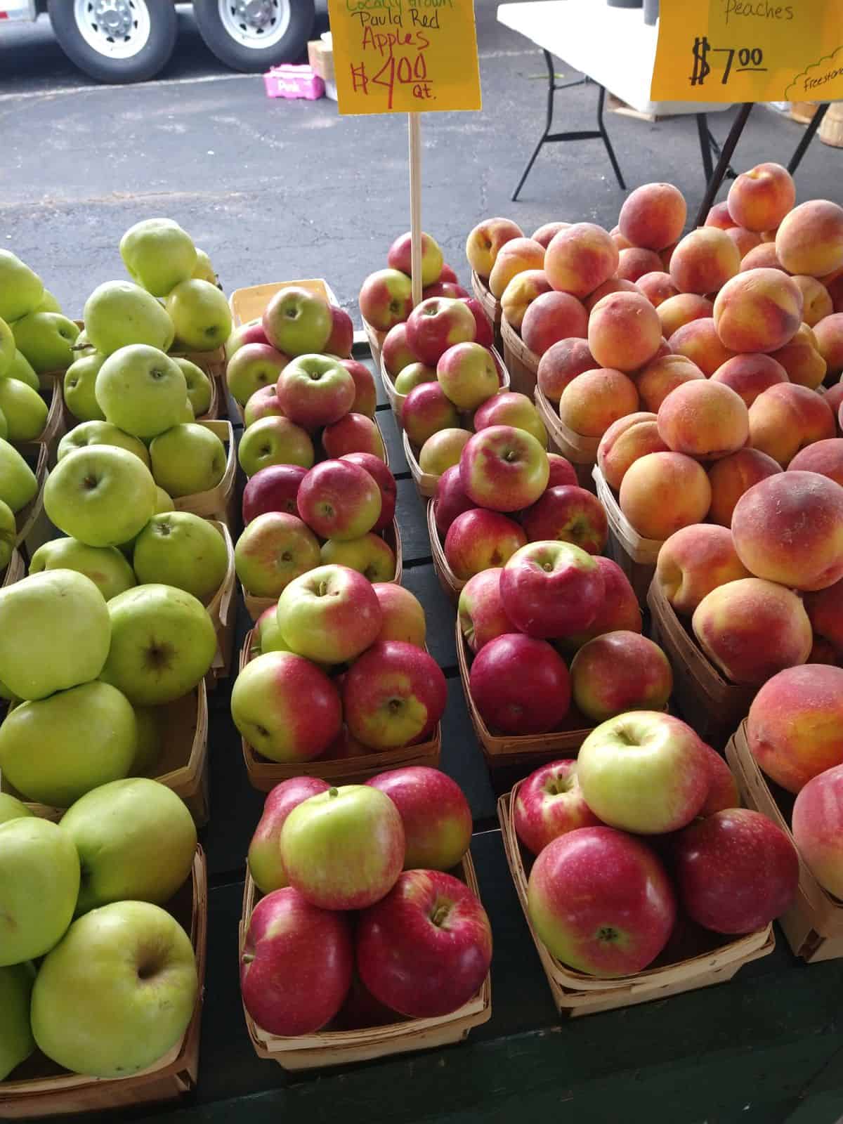 Paula Red apples at a farmers market next to Ginger Gold apples and peaches.