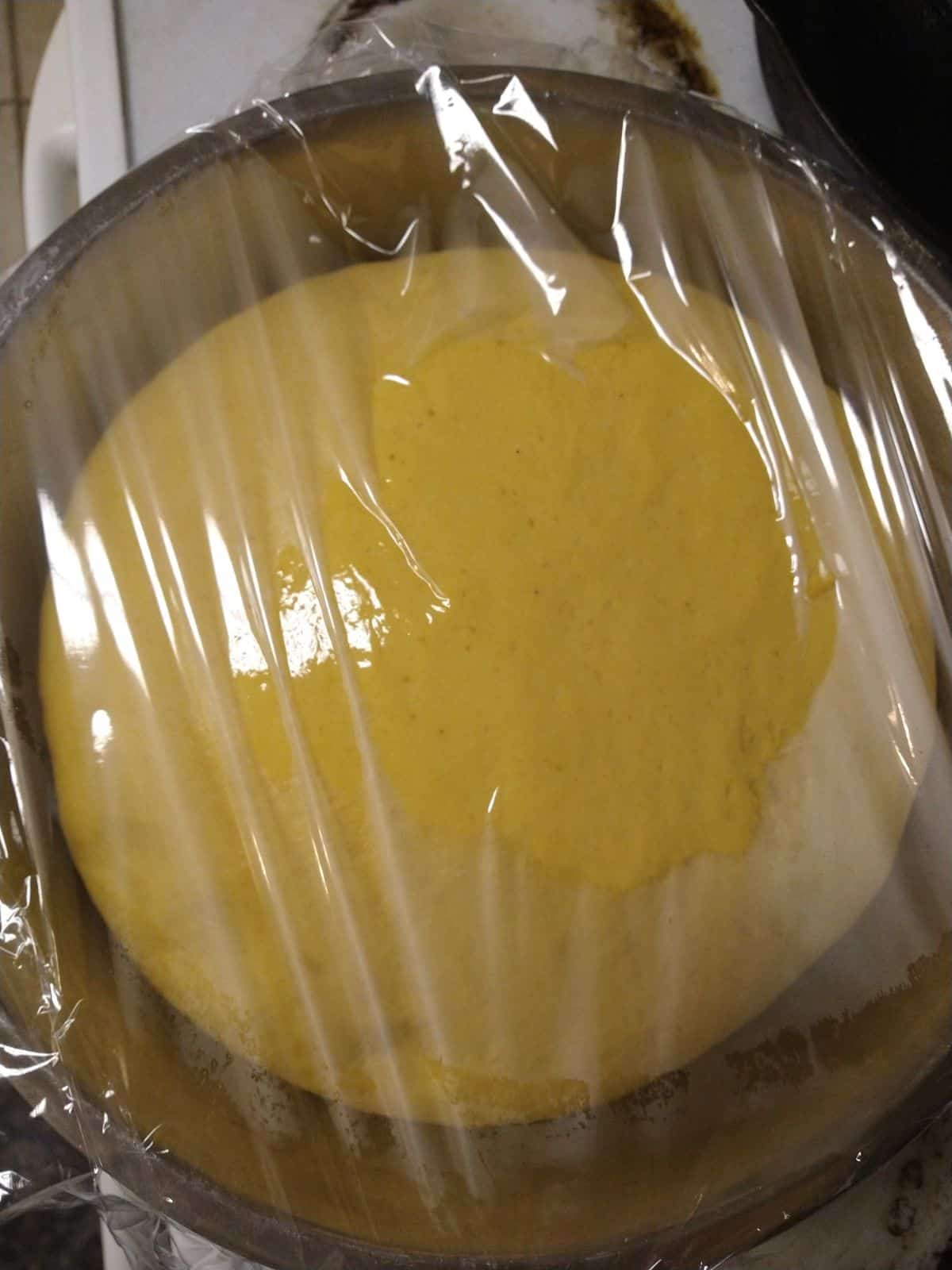 A pumpkin yeast dough in a mixing bowl covered with plastic wrap.