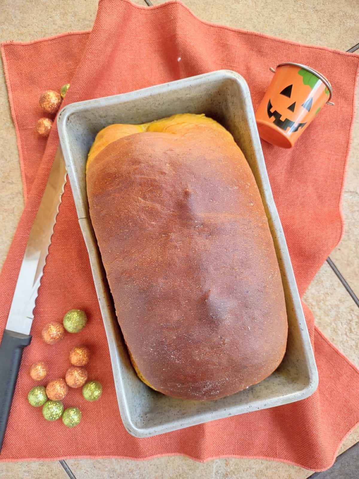 A loaf of pumpkin yeast bread in a metal loaf pan on a orange towel. 